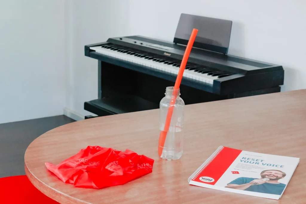 Ein Theraband, eine Flasche mit LaxVox-Schlauch so wie ein Singbuch sind auf einem Tisch.