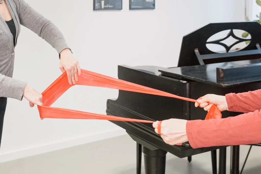 Zwei Personen ziehen ein rotes Theraband in entgegengesetzte Richtungen