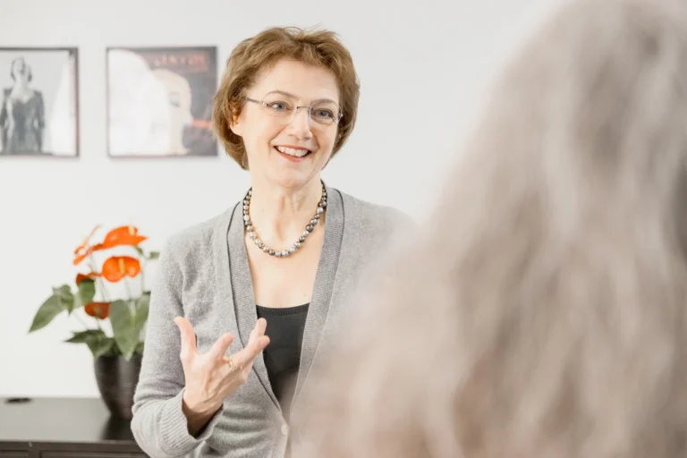 Eine Gesangspädagogin erklärt lächelnd etwas, während sie sich einer Patientin zuwendet.