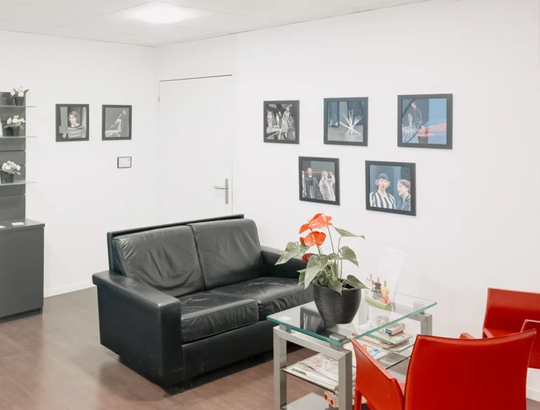 Wartebereich mit Sofa, Stuhl und gerahmten Bildern von Sängerinnen und Sängern an der Wand.