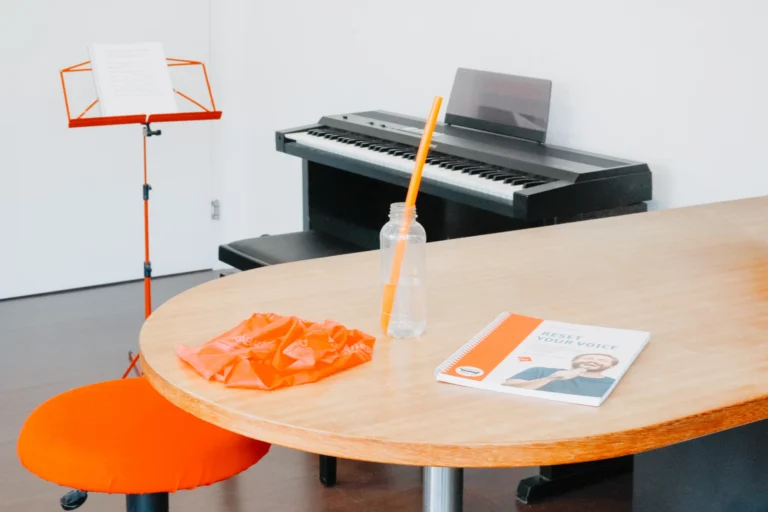 Therapieraum: Teraband, LaxVox und Singbuch auf dem Tisch, dahinter Notenständer und E-Piano.