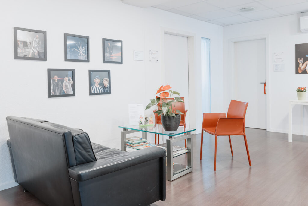 Wartebereich mit Sofa, Stuhl und einer Pflanze auf einem Tisch.